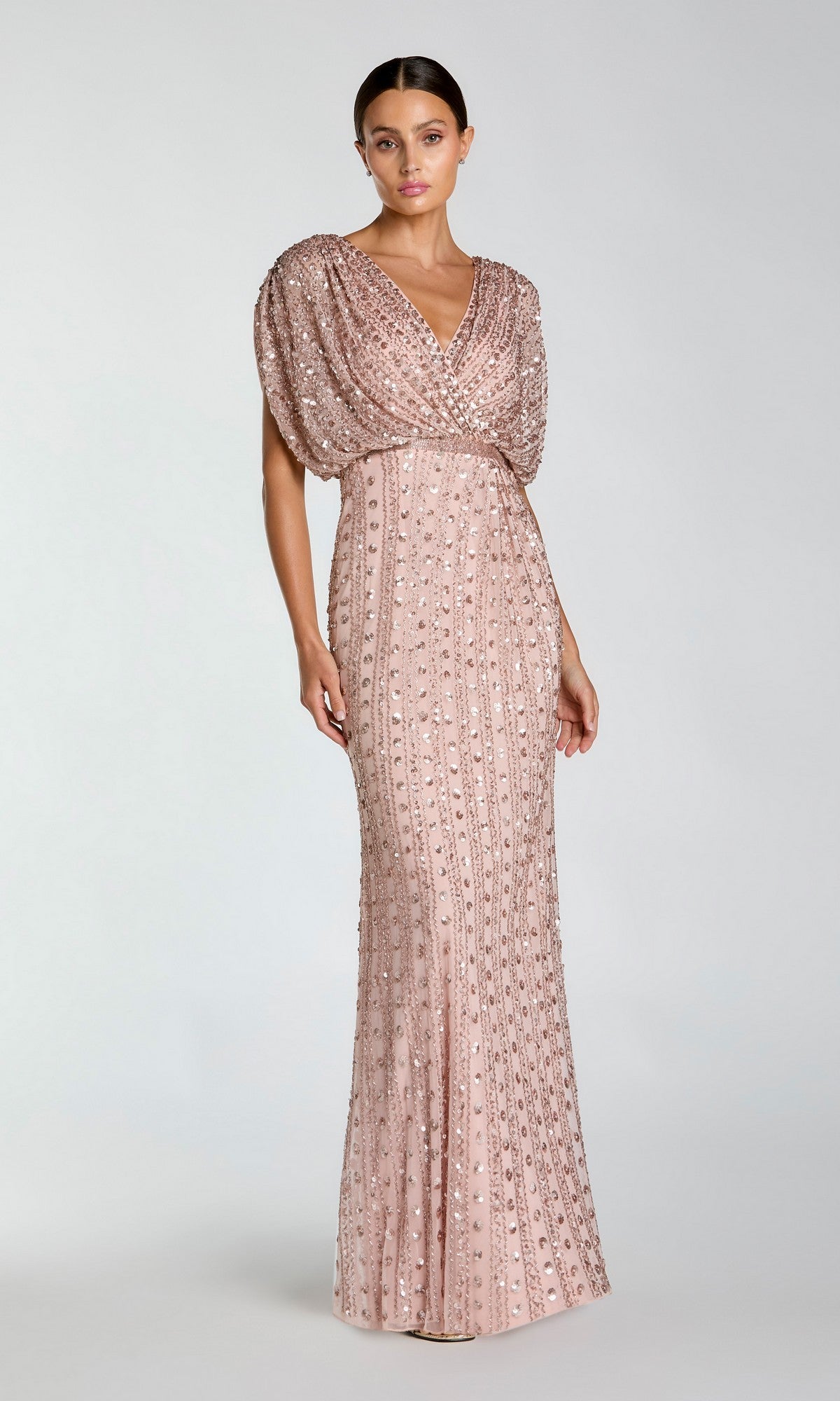 A woman stands wearing the Long Formal Dress: Mac Duggal 23081 in Vintage Rose, a floor-length, sequin-embellished gown featuring short draped sleeves and a v-neckline, set against a plain light background.